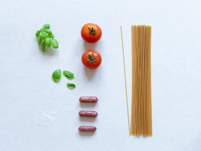 Tomate, albahaca, pasta y embutido preparados sobre una superficie clara.